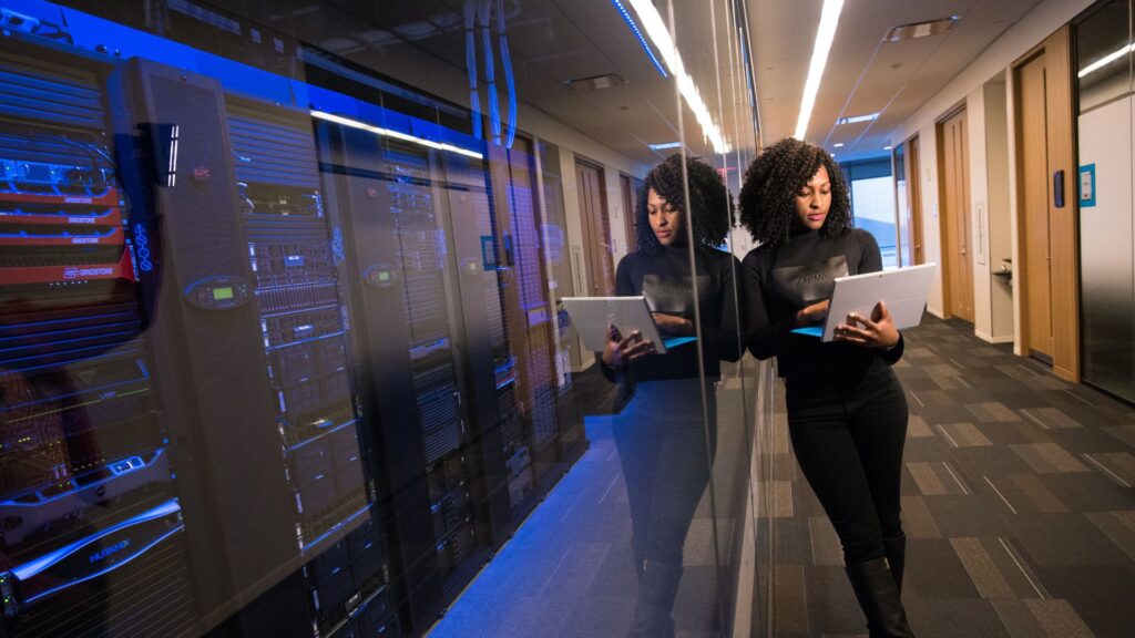 engineer standing by a server wall with computer in hand