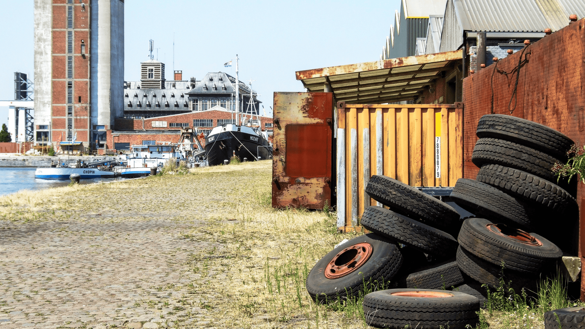 a pile of tires against a rusty fence at an industrial waterway