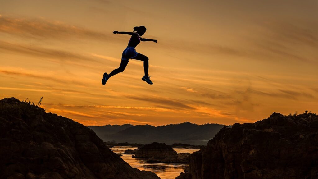 a woman leaping from one rock to another against a sunset background
